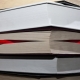 A red pencil, with a white rubber at the back, sticking out at both ends from a thick books with yellowed, dirty pages.